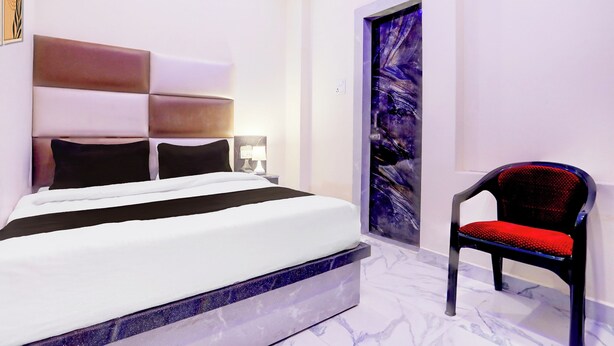 A modern hotel room with a bed, a chair, and a painting on the wall. - Super OYO Collection O Subedarganj (Prayagraj)