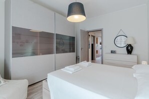 A hotel room with a bed, a bedside table with a lamp, a wardrobe, and a mirror. - A modern 57sqm flat, perfect for 4 guests, located on the first floor of a building with an elevator (stairs to reach it).The property is situated in the San Salvario district, one of Turin's central neighborhoods, renowned for its Art Nouveau and Baroqu (Turin)