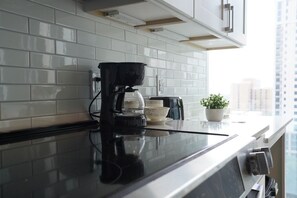 A kitchen with white subway tiles, a black coffee maker, a white bowl, and a potted plant on the counter. - Luxury High-Rise - Designer-Inspired Stay with City Views (Atlanta)