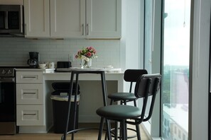 A kitchen with white cabinets, a coffee maker, a trash can, and a window with a view. - Luxury High-Rise - Designer-Inspired Stay with City Views (Atlanta)