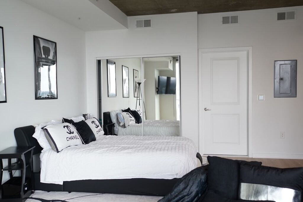 A bedroom with a bed, a desk, a chair, a wardrobe, a mirror, and a door.
