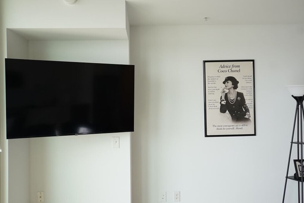 A room with a mounted flat-screen TV and a framed Coco Chanel advertisement on the wall.