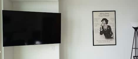 A room with a mounted flat-screen TV and a framed Coco Chanel advertisement on the wall.