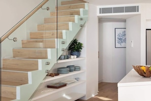 A modern staircase with glass railings and wooden steps, leading to a white interior space with a plant and decorative plates. - Aquamarine on Fairy Bower (Manly)