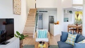 A modern living space with a staircase leading to a kitchen area, a dining table with chairs, and a sofa with cushions. - Aquamarine on Fairy Bower (Manly)
