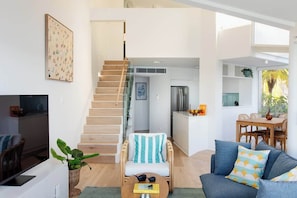 A modern living space with a staircase leading to a kitchen area, a dining table with chairs, and a sofa with cushions. - Aquamarine on Fairy Bower (Manly)