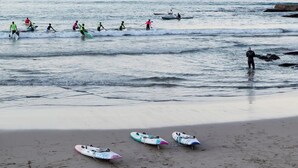 A beach with people paddling and standing in the water, and several surfboards on the sand. - Aquamarine on Fairy Bower (Manly)