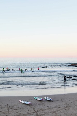 A beach with people paddling and standing in the water, and several surfboards on the sand. - Aquamarine on Fairy Bower (Manly)