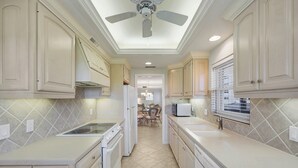 A kitchen with white cabinetry, a ceiling fan, and a tiled backsplash. - Harborside Gardens at the Moorings (Naples)