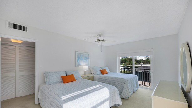A bedroom with two beds, a ceiling fan, a window with a view, and a door with a closet. - Harborside Gardens at the Moorings (Naples)