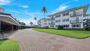 A residential building with a covered driveway, a well-maintained lawn, and a clear sky. - Harborside Gardens at the Moorings (Naples)