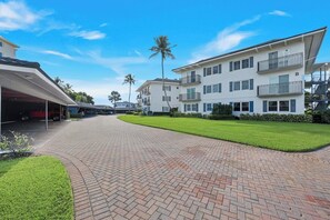 A residential building with a covered driveway, a well-maintained lawn, and a clear sky. - Harborside Gardens at the Moorings (Naples)