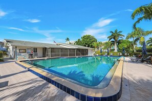 A swimming pool with a tiled edge, a covered area with chairs, and palm trees in the background. - Harborside Gardens at the Moorings (Naples)