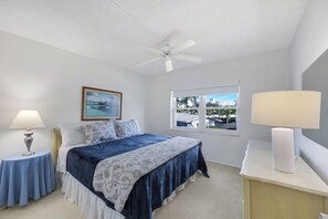 A bedroom with a bed, a ceiling fan, a window with a view, and two bedside tables with lamps. - Harborside Gardens at the Moorings (Naples)