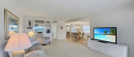 A living room with a white sofa, a television, and a dining area with chairs and a table.