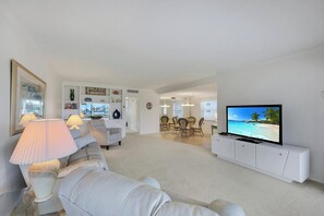 A living room with a white sofa, a television, and a dining area with chairs and a table. - Harborside Gardens at the Moorings (Naples)