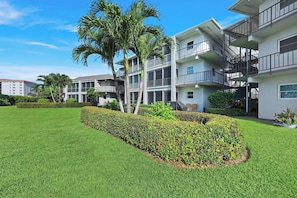 A multi-story residential building with balconies, a well-maintained lawn, and palm trees. - Harborside Gardens at the Moorings (Naples)