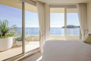 Een slaapkamer met een groot bed, een balkon met plantenbakken en uitzicht op zee.