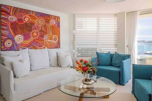 A modern living room with a white sofa, a teal sofa, and a glass coffee table with flowers. - Luxury Waterfront Living at Fairy Bower (Manly)