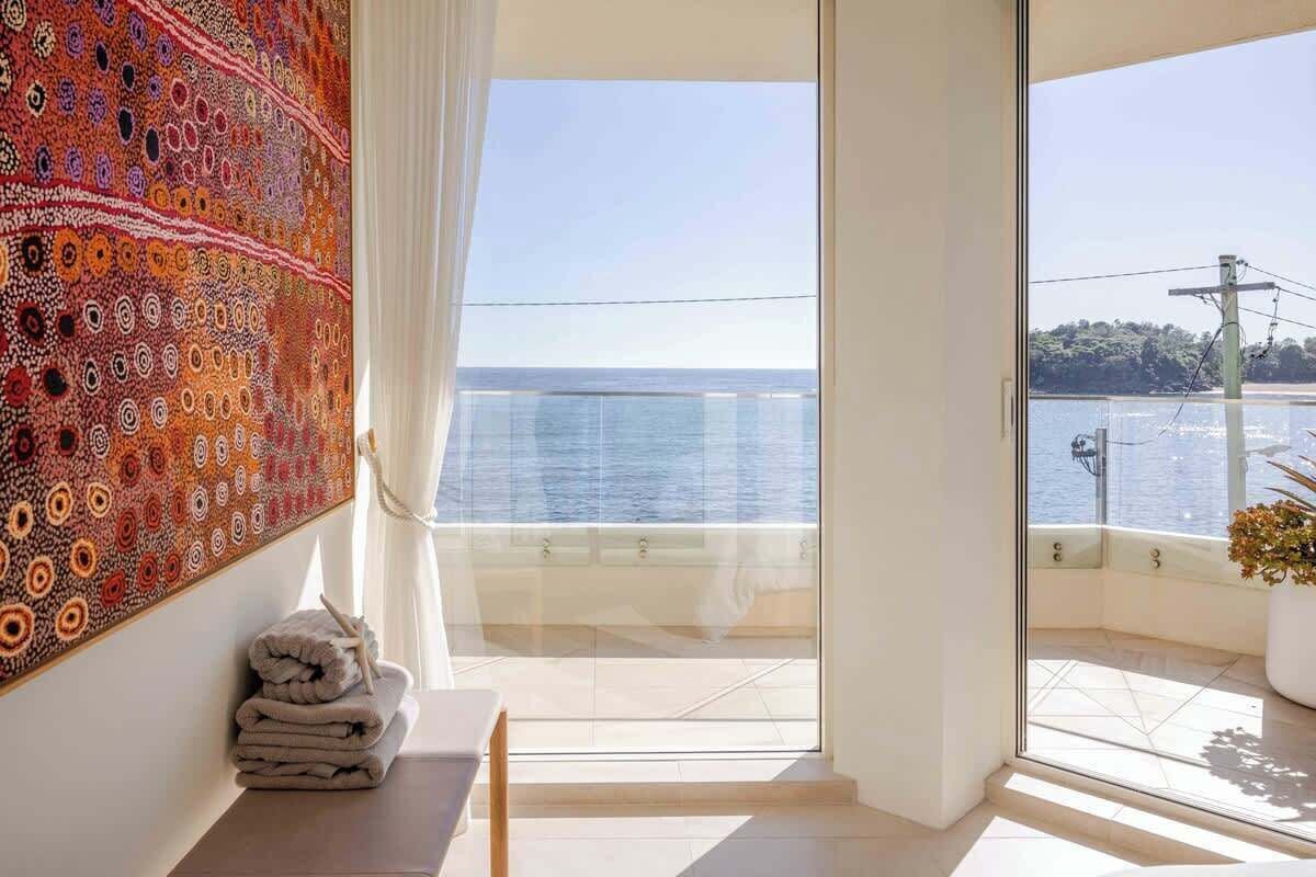 A room with a large window overlooking a body of water, a patterned tapestry on the wall, and a stack of towels.