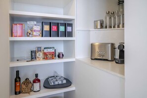 A kitchen with shelves containing tea tins, a coffee machine, and various food items. - Luxury Waterfront Living at Fairy Bower (Manly)