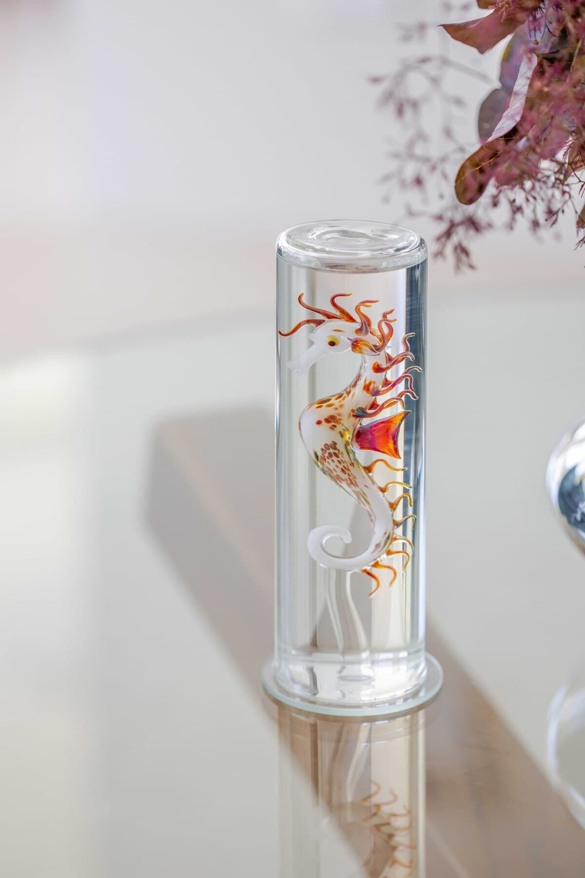 A clear glass vase with a seahorse design on a reflective surface.