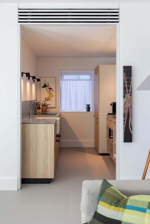 A compact kitchen with a central island, a window with curtains, and a small dining area. - Bower Break at Fairy Bower (Manly)