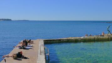 A pier with clear water, people sunbathing, and a sculpture.