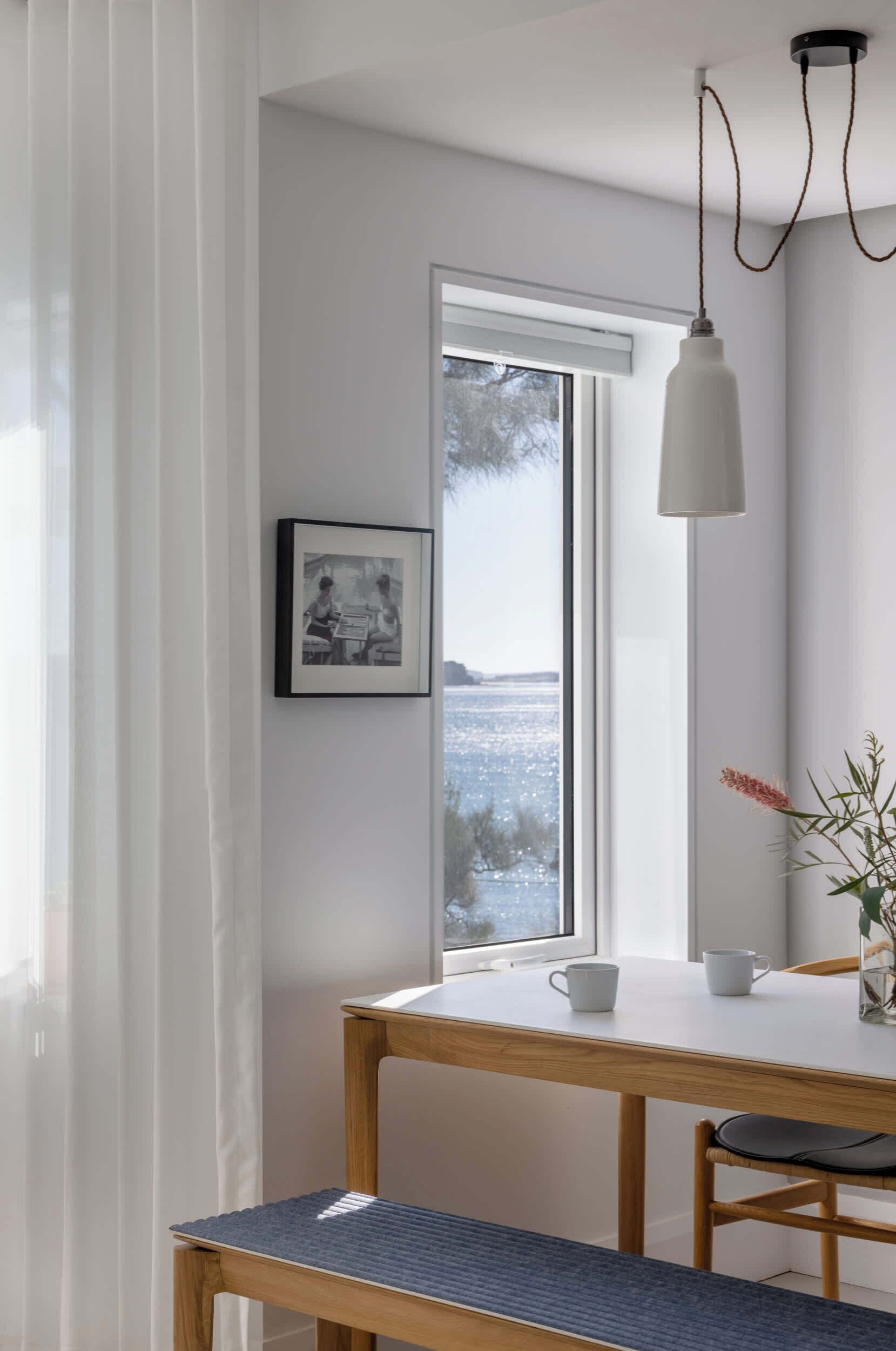 A dining area with a table, chairs, a bench, a picture on the wall, a window with a view, and a pendant light.