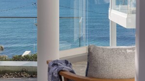 En balkong med fri utsikt över havet, en vit stol och ett glasräcke.