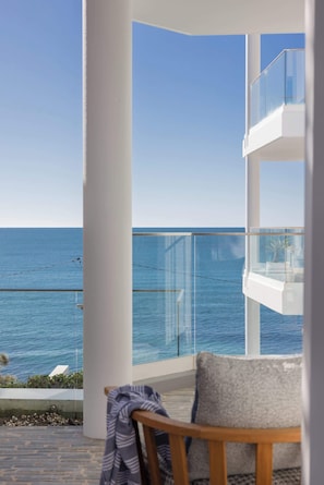 A balcony with a clear view of the sea, a white chair, and a glass railing. - Bower Break at Fairy Bower (Manly)