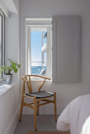 A room with a wooden chair, a window with a view of a building, and a white door. - Bower Break at Fairy Bower (Manly)