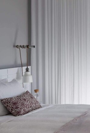 A neatly made bed with a patterned pillow, a wall-mounted lamp, and a window with vertical blinds. - Bower Break at Fairy Bower (Manly)