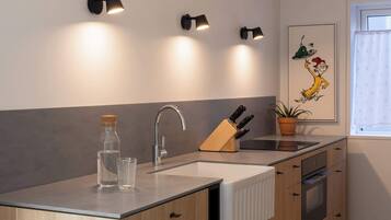 A modern kitchen with a built-in island, a sink, and a stove. There are wall-mounted lights above the island and a framed picture on the wall.
