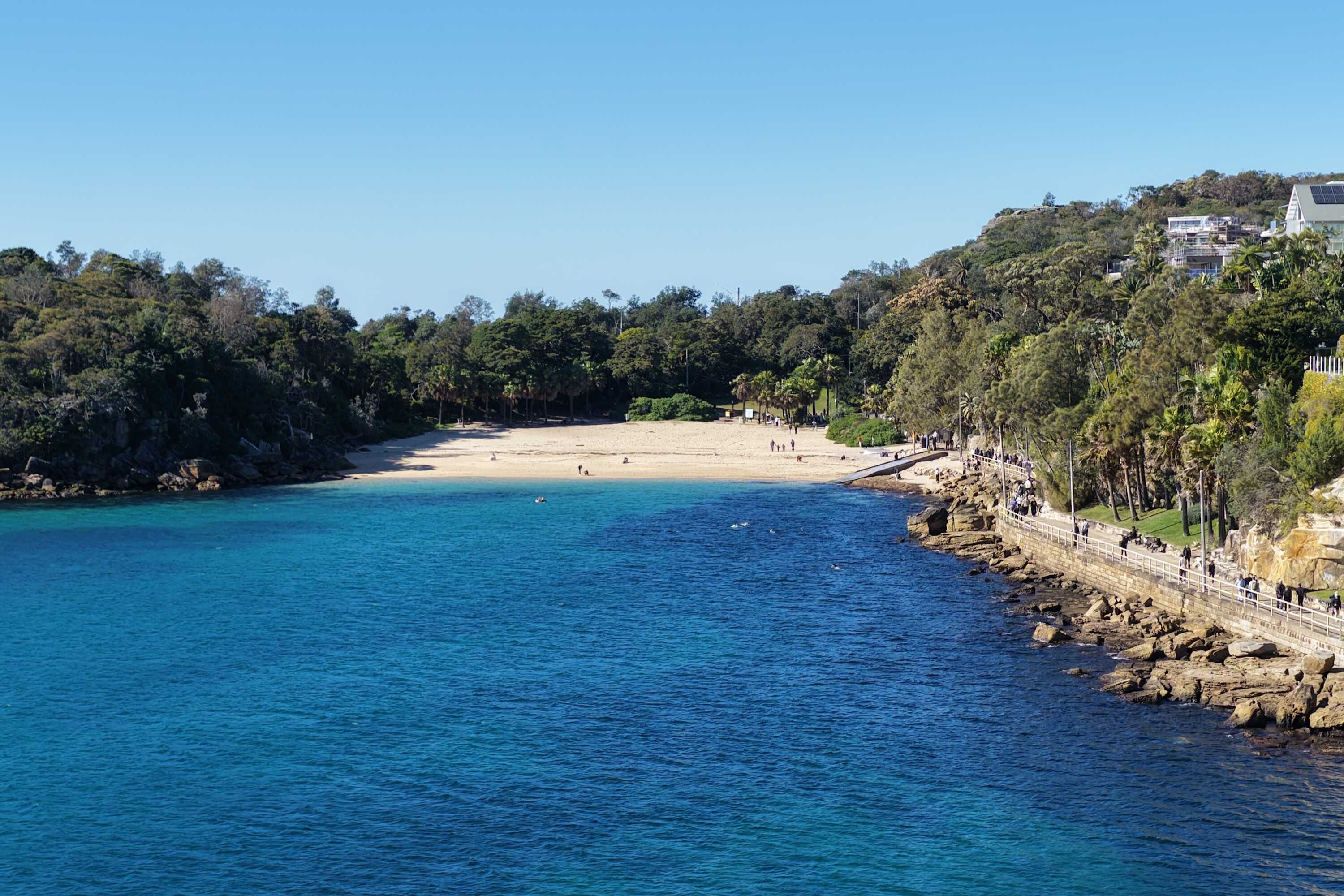 A coastal beach with clear blue waters, a sandy shore, and a rocky coastline.