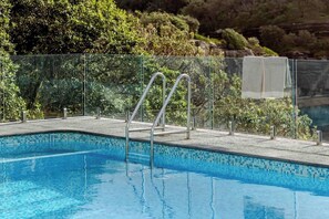 Ein klares, blaues Schwimmbecken mit Glasgeländer und Metallstufen zum Wasser.
