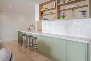 Eine moderne Küche mit Marmorarbeitsplatte, grünen Schränken und einer Bar mit Barhocker.