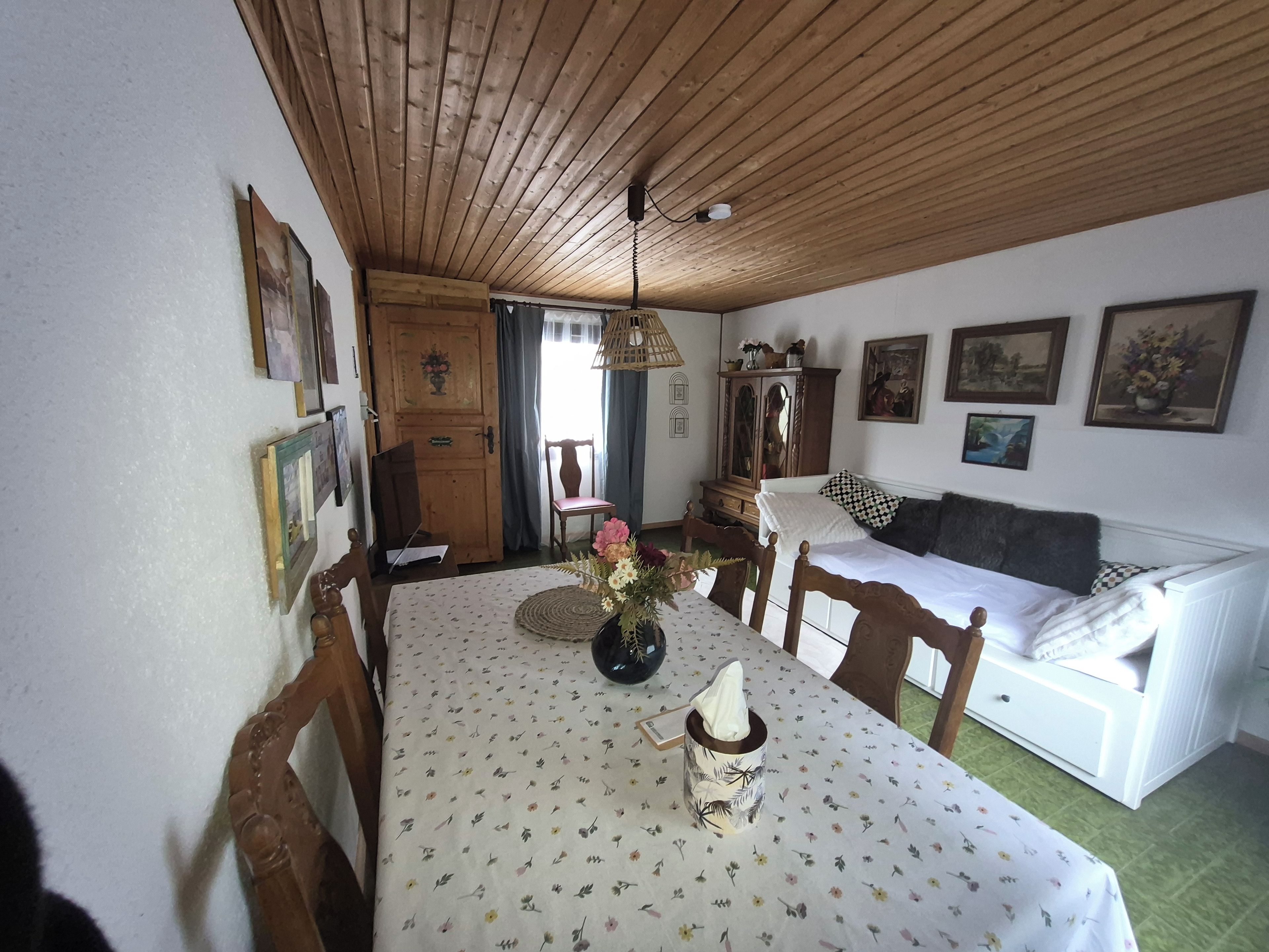 Een eetgedeelte met een houten plafond, een witte tafel met een bloemrijk tafelkleed en een witte bank op de achtergrond.