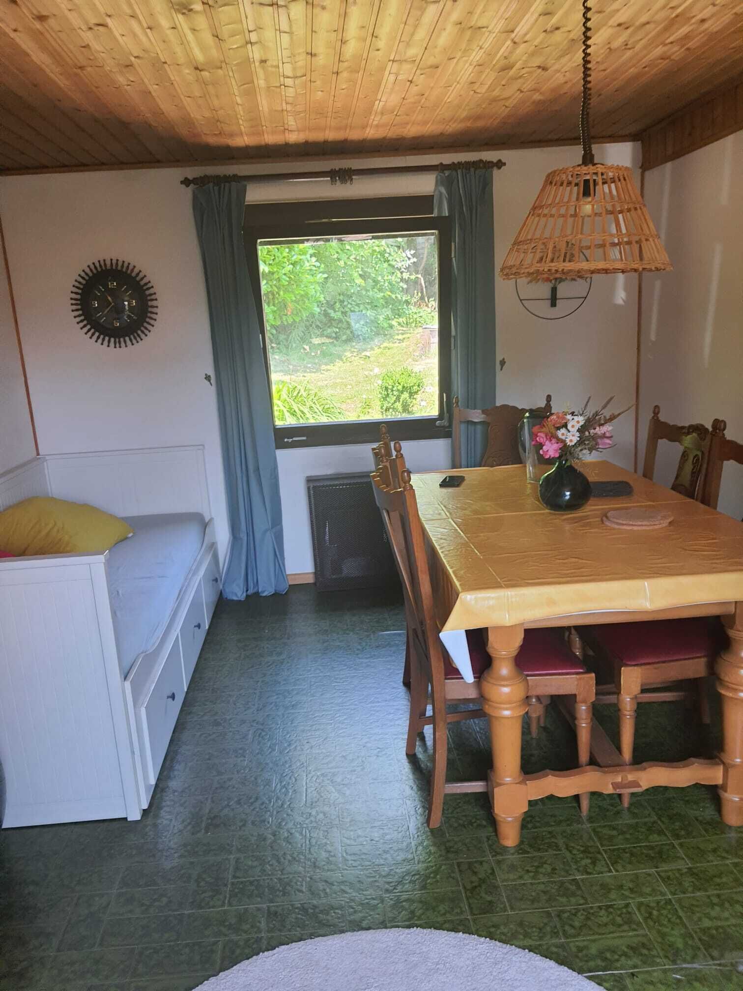 A dining area with a wooden table, chairs, a vase with flowers, a clock on the wall, and a window with curtains.
