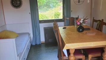 A dining area with a wooden table, chairs, a vase with flowers, a clock on the wall, and a window with curtains.