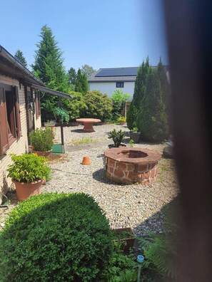 A courtyard with a brick fire pit, potted plants, and a building with a tiled roof.