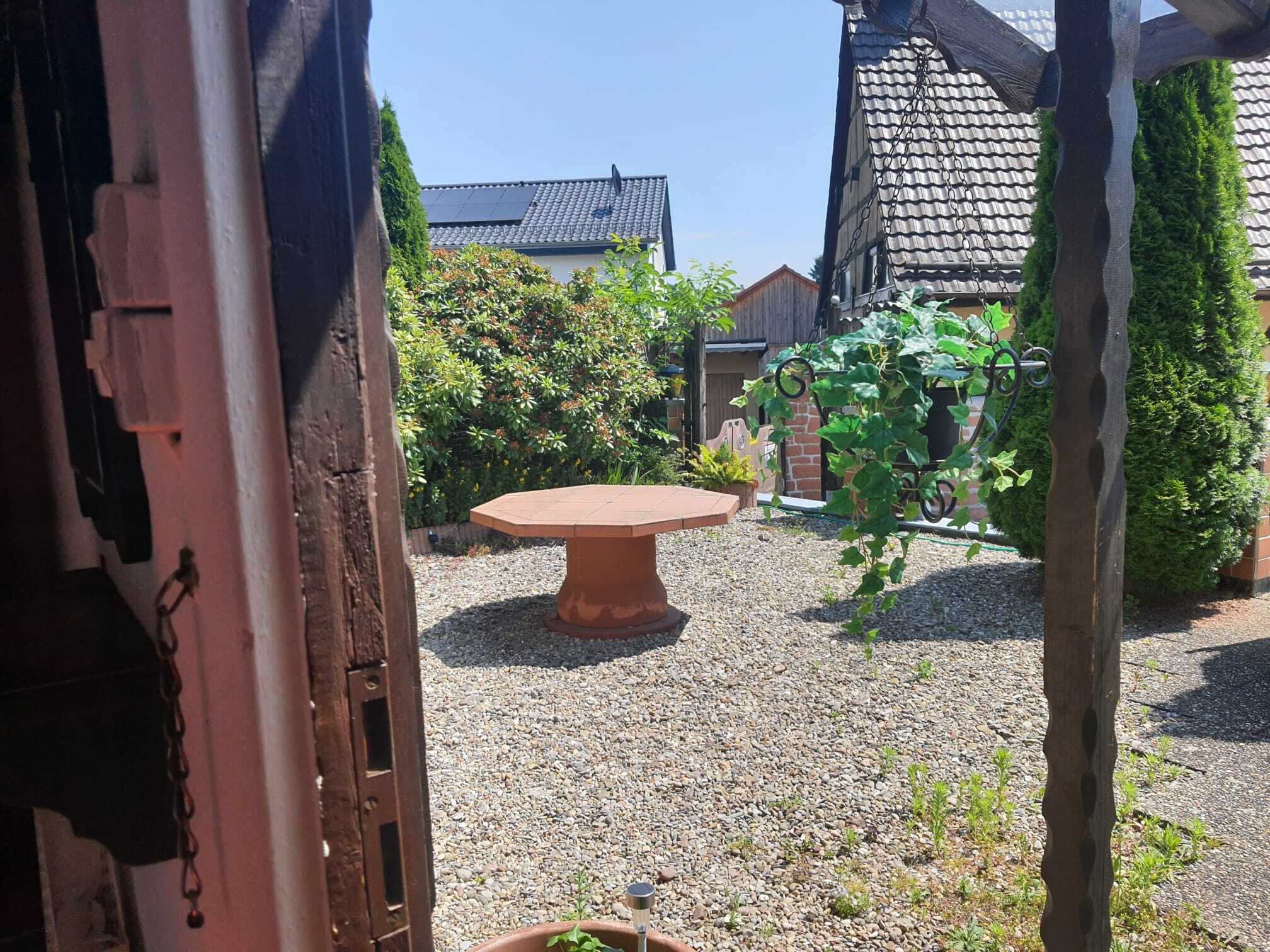 Une cour avec une table ronde, un sol recouvert de gravier et, au fond, un bâtiment doté d’un toit en tuiles.