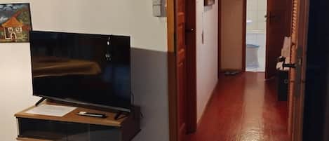 A room with a television on a wooden stand, a white rug, and a hallway leading to a bathroom.