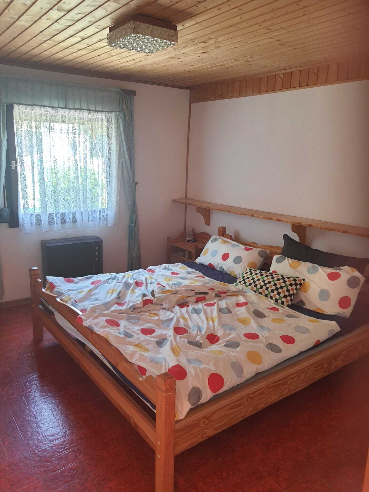 Una cama de madera con una colcha de lunares, una mesita de noche y un ventanal con cortinas.