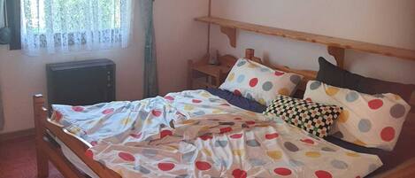 Una cama de madera con una colcha de lunares, una mesita de noche y un ventanal con cortinas.