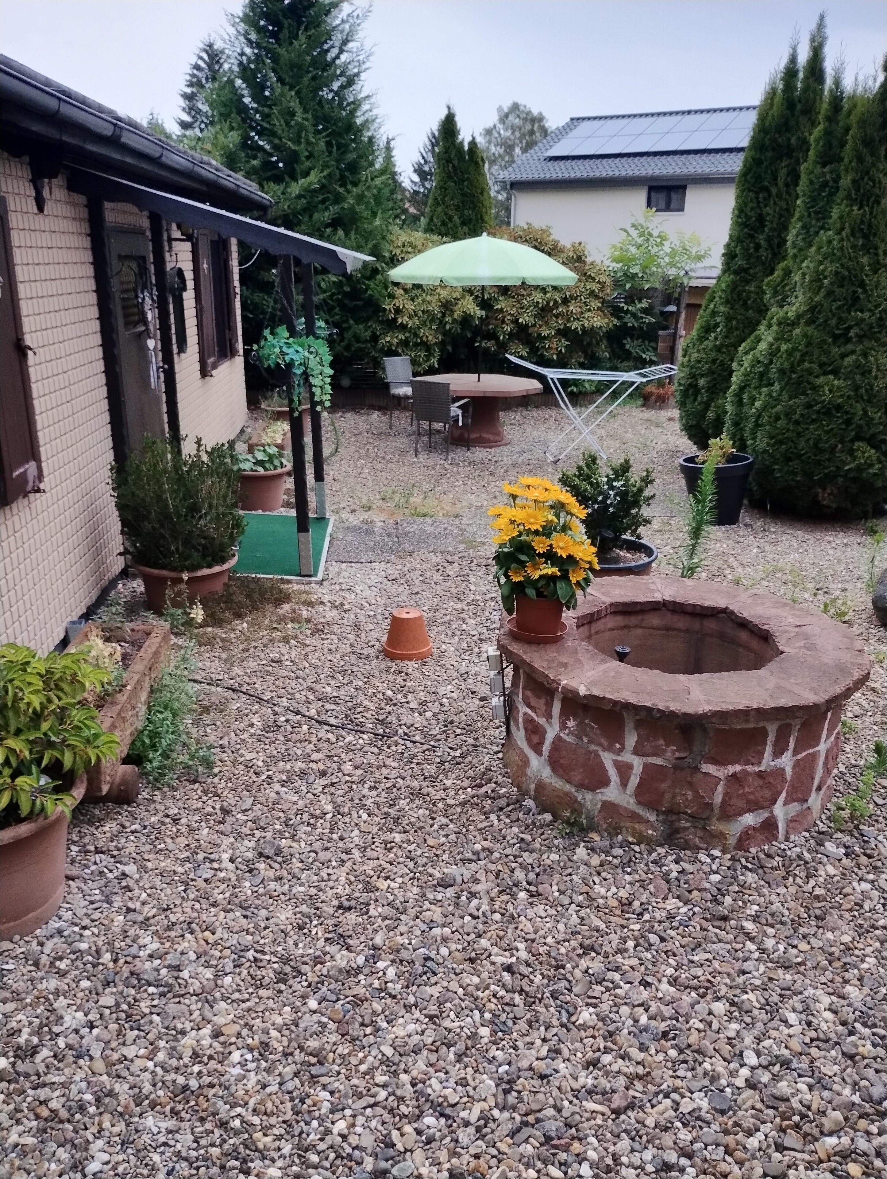 Een patio met grind, een vuurkuil van steen, potplanten en tuinmeubilair.