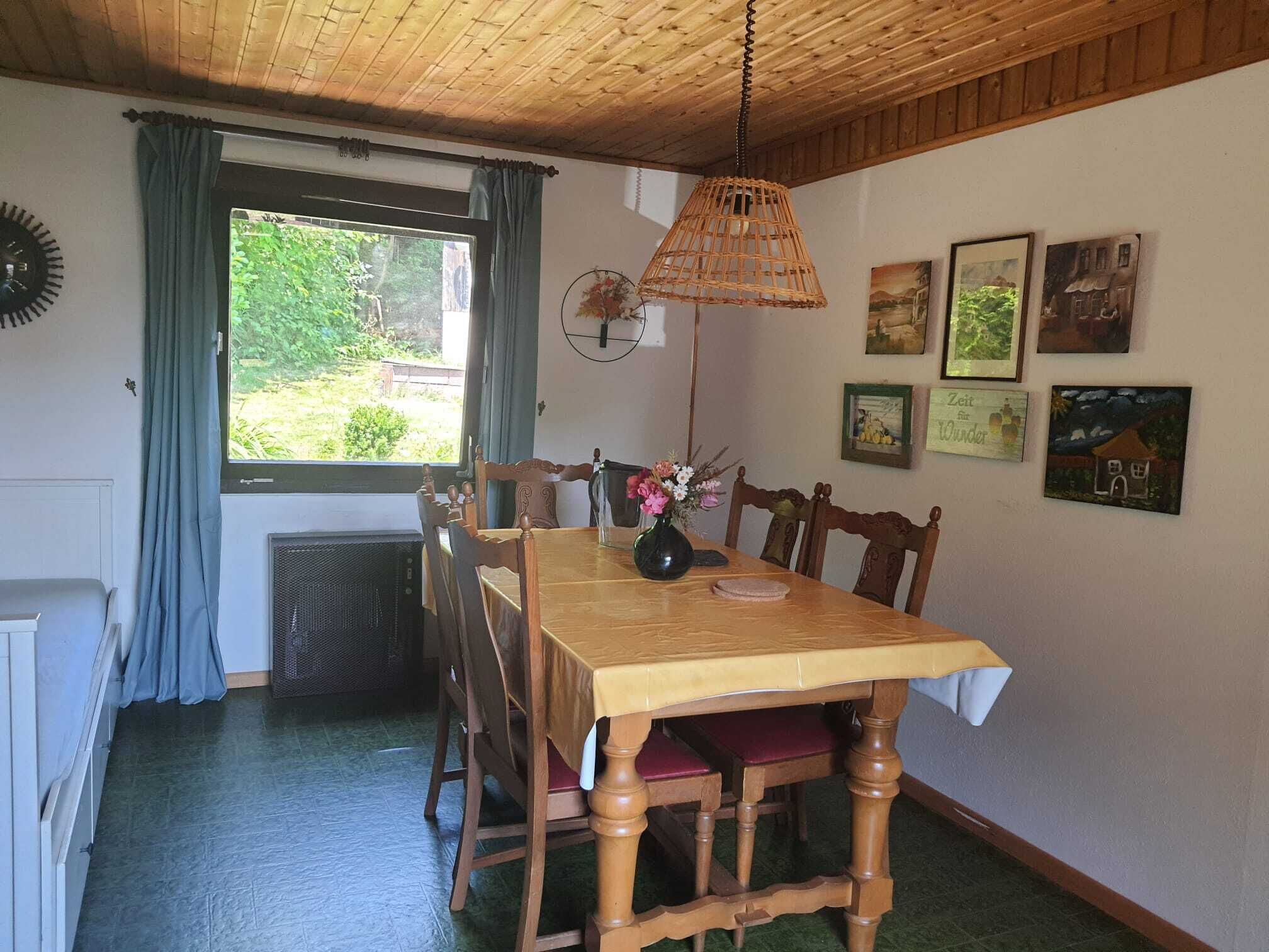 Ein Essbereich mit einem Holztisch und Stühlen, einer Pendelleuchte sowie gerahmten Bildern an der Wand.