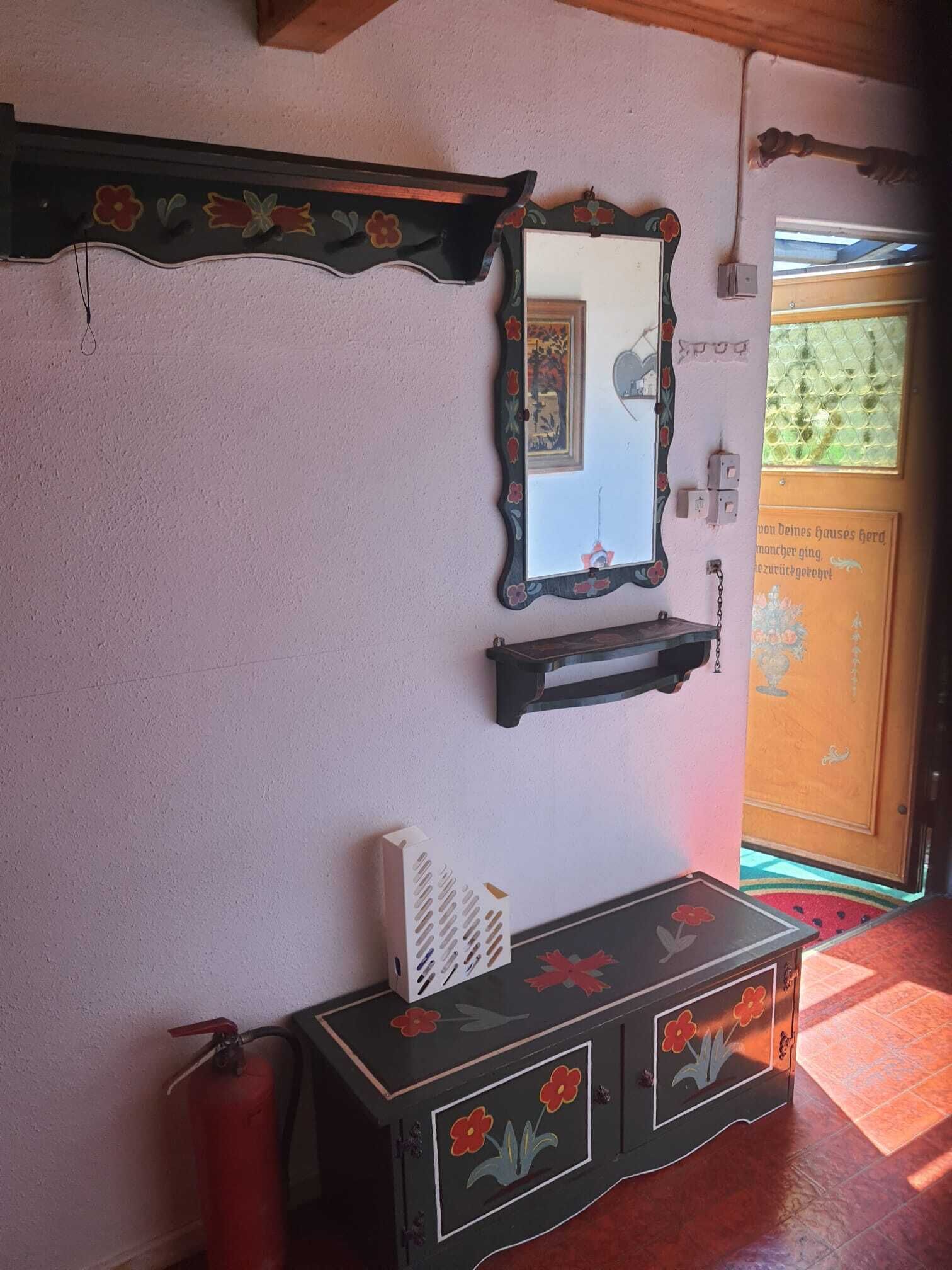 A room with a wooden ceiling, a mirror with floral designs, a small shelf, and a fire extinguisher.