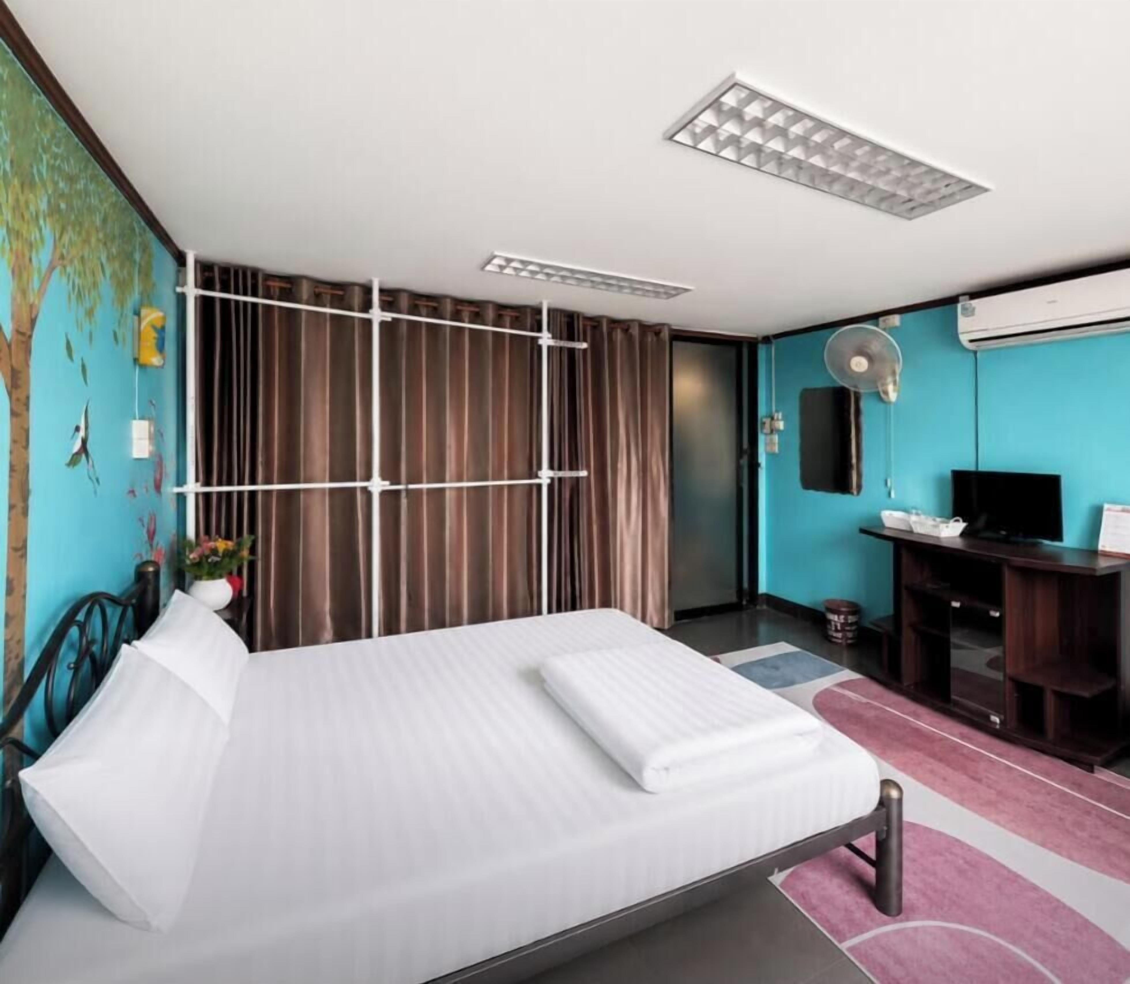 A hotel room with a bed, curtains, a desk with a chair, a television, and a wall-mounted air conditioning unit.