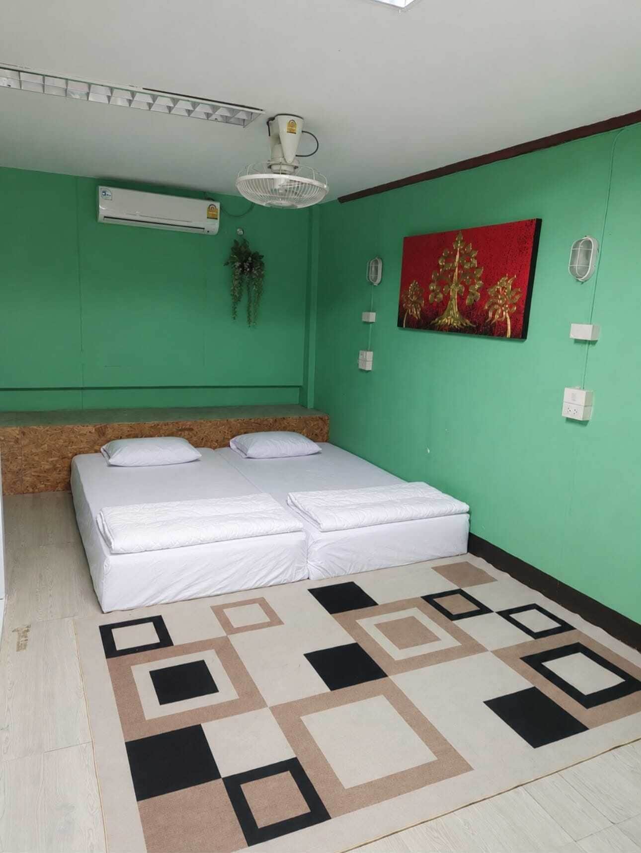 A room with a bed, a ceiling fan, an air conditioning unit, a wall-mounted light, and a decorative painting.
